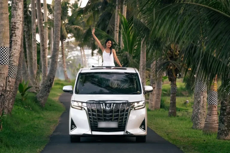 Guest waving from the sunroof of an Alphard on a palm-lined drive in Bali